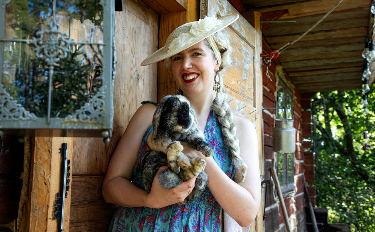 Kuvassa hymyilevä vaalea nainen pitää sylissään mustavalkoista kania.